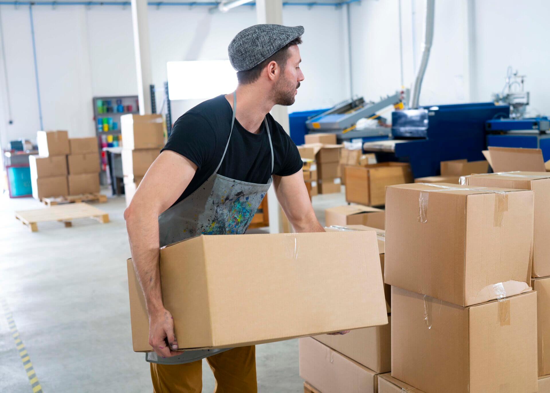 Young man holding carboard boxes stacked at industrial warehouse